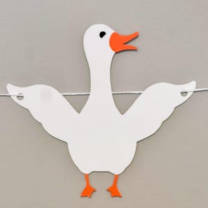 May include: White paper cutout of a goose with orange beak and feet. The goose is hanging from a string.