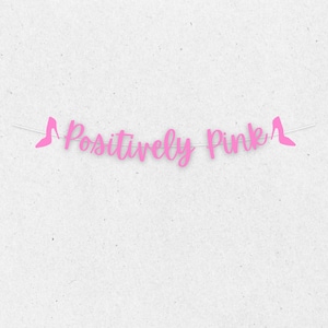 Puede incluir: Pancarta rosa con el texto "Positively Pink" y recortes de zapatos de tac&oacute;n alto rosas en cada extremo.