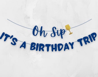 Op de afbeelding: Blauwe banner met de tekst "Oh Sup It's a Birthday Trip" en een gouden glitter wijnglas.