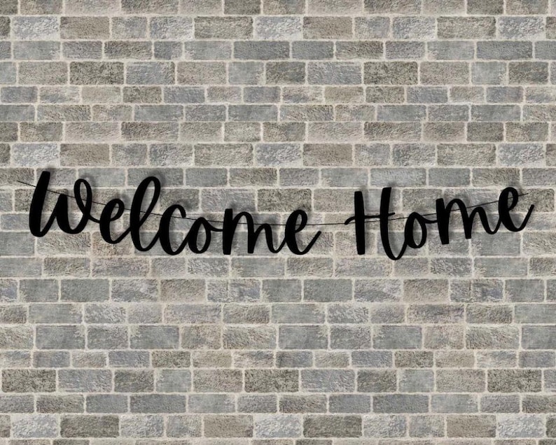 May include: Black welcome home banner hanging on a brick wall.