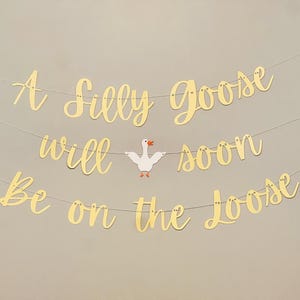 May include: A gold banner with the text "A Silly Goose Will Soon Be On The Loose" with a white goose cutout in the middle.