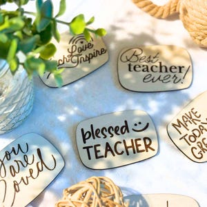 May include: Wooden rectangular plaques with inspirational quotes, including "Love & Inspire," "Best teacher ever!," "Blessed TEACHER," "Make Today Great," and "You are loved." The plaques are light-colored with dark brown lettering.