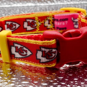 May include: Red and yellow dog collar featuring the Kansas City Chiefs logo. The collar has a red plastic buckle and a yellow plastic adjustment piece. The collar is approximately 1 inch wide.