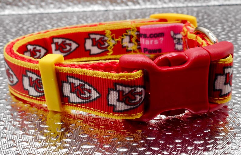 May include: Red and yellow dog collar featuring the Kansas City Chiefs logo. The collar has a red plastic buckle and a yellow plastic adjustment piece. The collar is approximately 1 inch wide.