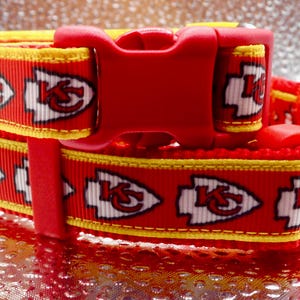 May include: Two red and yellow dog collars with the Kansas City Chiefs logo. The collars have a red plastic buckle and a yellow accent. The Chiefs logo is white with a red outline. The collars are stacked on top of each other.