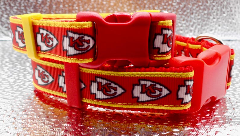 May include: Two red and yellow dog collars with the Kansas City Chiefs logo. The collars have a red plastic buckle and a yellow accent. The Chiefs logo is white with a red outline. The collars are stacked on top of each other.