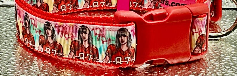May include: Red dog collar featuring a repeating pattern of a person in a football jersey with the number 87. The collar has a red plastic buckle and a silver metal D-ring for leash attachment.