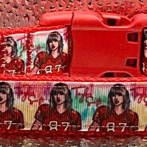 May include: Red dog collar featuring a repeating pattern of a person in a red football jersey with the number 87. The collar has a red plastic buckle and a metal D-ring.