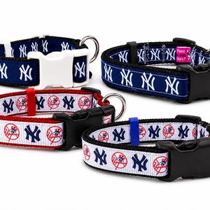 May include: Four dog collars featuring the New York Yankees logo. Two collars are navy blue with white logos, and two are white with red accents and logos. Each collar has a plastic buckle and a metal D-ring.