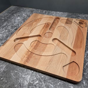 Könnte beinhalten: Ein hölzernes Servierbrett mit geschnitzten kreisförmigen und gebogenen Rillen. Auf dem Brett steht der Text "Dutch warming board Oven Travo". Das Brett ist aus hellem Holz gefertigt.