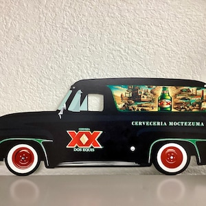 May include: Black vintage-style metal sign shaped like a truck. The sign features the Dos Equis logo and the words "CERVECERIA MOCTEZUMA." The truck's window displays a colorful scene with a beer bottle.