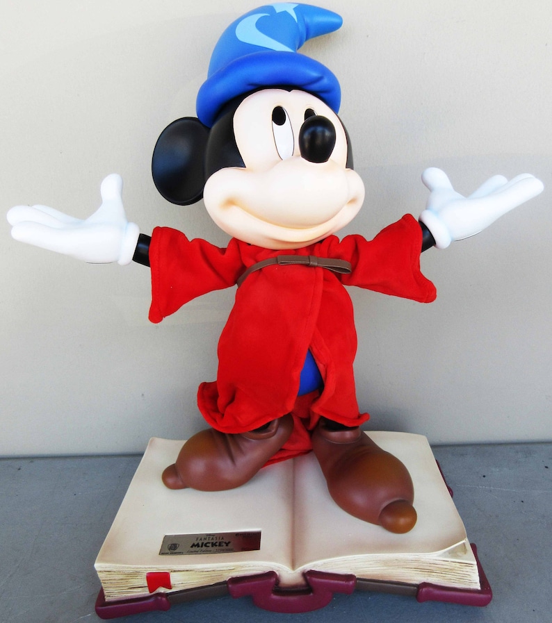 May include: A red and blue sorcerer Mickey Mouse figurine standing on a large open book with the text "Fantasia Mickey" on the front cover.