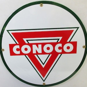 May include: A round, white, metal sign with a green border and a red triangle with a white outline. The triangle has a white "CONOCO" in the center.