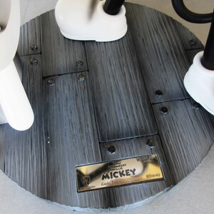 May include: A black and white Mickey Mouse figurine with a gold plaque that reads "Disney Steamboat Willie Mickey Limited Edition" and "&copy;Disney". The figurine is standing on a wooden base with black screws.