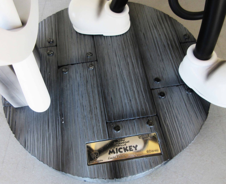 May include: A black and white Mickey Mouse figurine with a gold plaque that reads "Disney Steamboat Willie Mickey Limited Edition" and "&copy;Disney". The figurine is standing on a wooden base with black screws.