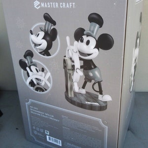 May include: A black and white figurine of Mickey Mouse as Steamboat Willie. The figurine is holding a ship's wheel and is standing on a wooden base. The box is labeled "Master Craft Mickey" and "MC-093 Steamboat Willie".