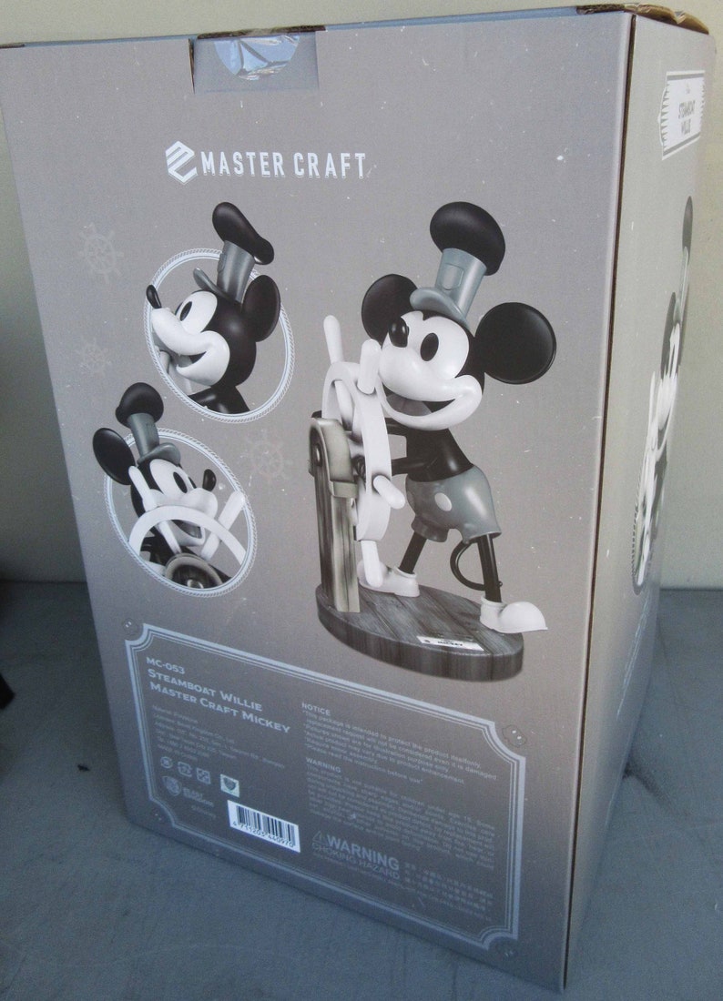 May include: A black and white figurine of Mickey Mouse as Steamboat Willie. The figurine is holding a ship's wheel and is standing on a wooden base. The box is labeled "Master Craft Mickey" and "MC-093 Steamboat Willie".