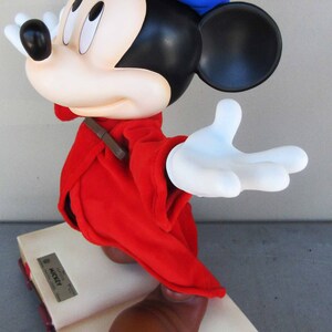May include: A red and blue Mickey Mouse figurine wearing a blue wizard hat with a white star. The figurine is standing on a closed book with the text "Limited Edition Mickey" on the cover.