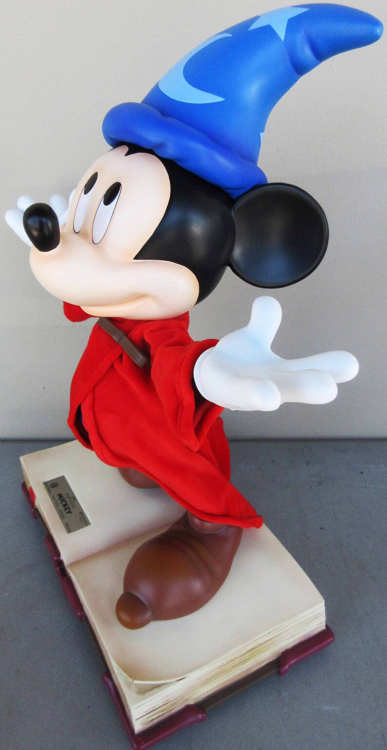 May include: A red and blue Mickey Mouse figurine wearing a blue wizard hat with a white star. The figurine is standing on a closed book with the text "Limited Edition Mickey" on the cover.