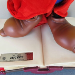 May include: A brown and red Mickey Mouse figurine standing on a closed book. The book is cream coloured with a gold label that reads "Disney Fantasia Mickey Limited Edition - 1/1500/2000 &copy;Disney".
