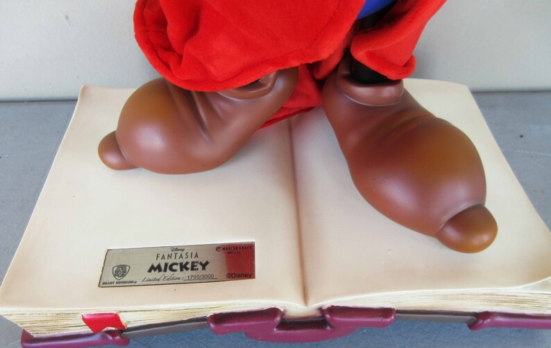 May include: A brown and red Mickey Mouse figurine standing on a closed book. The book is cream coloured with a gold label that reads "Disney Fantasia Mickey Limited Edition - 1/1500/2000 &copy;Disney".