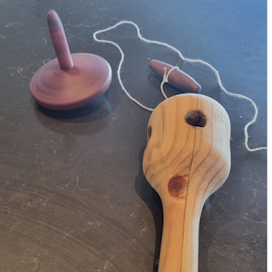 May include: A wooden toy set comprising a spinning top, a yo-yo, and a wooden handle. The spinning top is a dark reddish-brown colour, while the yo-yo and handle are light-coloured wood. A white string connects the yo-yo to the handle.