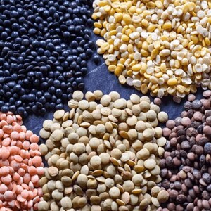 May include: A close-up view of six different types of lentils: black, red, green, brown, yellow, and split. The lentils are arranged in a circle on a dark gray surface.