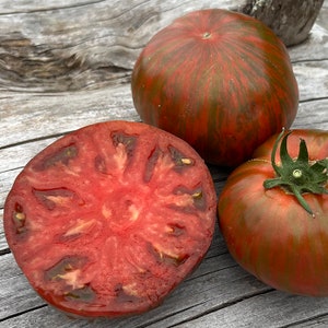 May include: Two whole heirloom tomatoes and one sliced tomato. The tomatoes are dark red with green and black stripes. The sliced tomato shows the red flesh and black seeds.