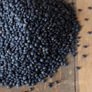 May include: A close-up view of a pile of black lentils on a wooden surface.