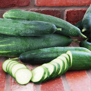 May include: A close-up of a pile of fresh, green cucumbers. The cucumbers are arranged in a pile, with some sliced cucumbers in the foreground. The cucumbers are a vibrant green color and have a smooth, shiny skin.