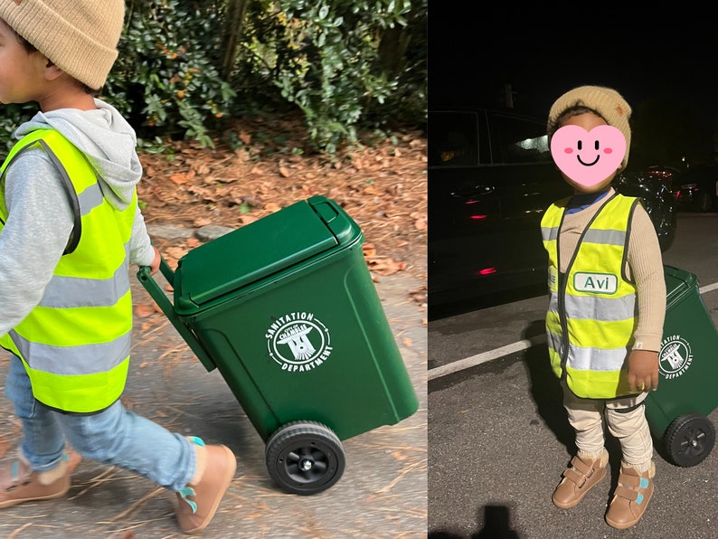 May include: Two children dressed in green and yellow safety vests, one pushing a green sanitation cart with a city logo, the other standing next to a similar cart. Both children are wearing hats and smiling.