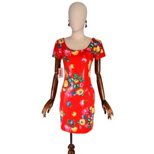 Può includere: Abito rosso con paillettes e motivo floreale. L'abito presenta uno scollo tondo e maniche corte. Il design floreale comprende fiori gialli, rosa e blu. L'abito è esposto su un manichino.
