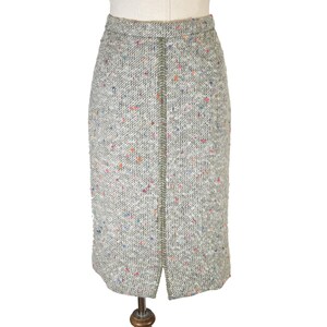 May include: A light gray tweed pencil skirt with a front slit. The skirt is speckled with colorful flecks of blue, orange, and pink. The skirt is displayed on a mannequin.