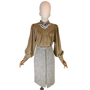 May include: A vintage olive green blouse with long sleeves and a button-down front is paired with a gray tweed pencil skirt. The skirt has a front slit and is speckled with colorful threads. A pearl necklace and gold earrings complete the outfit.