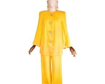 May include: A bright yellow two-piece suit displayed on a mannequin. The jacket has three decorative buttons and wide sleeves. The pants are wide-legged. The suit has a textured trim on the jacket and pants. Gold-colored earrings are also displayed.