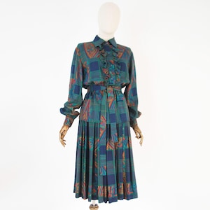 Peut inclure: Un ensemble deux pièces composé d'une chemise à manches longues boutonnée avec un plastron à volants et d'une jupe midi plissée assortie. Les deux pièces présentent un motif géométrique bleu marine, bleu sarcelle et orange avec une ceinture.