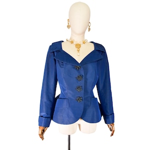 May include: A royal blue blazer with a notched collar, long sleeves, and decorative black buttons. The jacket features two front pockets and is displayed on a mannequin. A gold necklace and earrings complete the ensemble.
