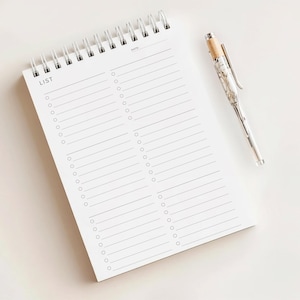 May include: A white spiral-bound notepad with the word "LIST" printed at the top left. The notepad has horizontal lines and circles for checklists. A silver pen with a wood-tone top rests beside the notepad.