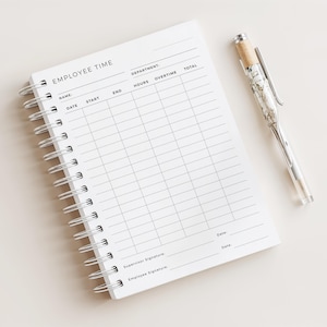 May include: A white spiral-bound notebook with the words "EMPLOYEE TIME" at the top. The notebook has columns for name, date, start, end, hours, overtime, and total. A clear pen with a marbled design rests beside the notebook.