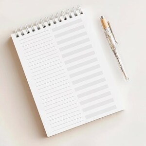 May include: A white spiral-bound notebook with lined and blank sections, and a silver pen with a wood-tone top. The notebook is open, and the pen is resting on a white surface.