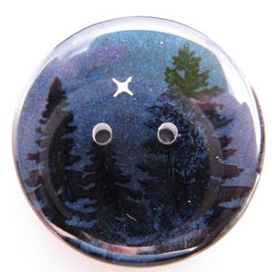 May include: A round button with a night sky design. The button features a dark blue background with a forest silhouette and a white star. Two holes are visible for sewing.
