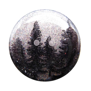May include: A round, two-hole button featuring a dark, glittery background with a silhouette of black pine trees. The surface has a smooth, glossy finish, and the overall design creates a shimmering effect across the circular button face.
