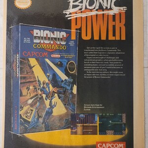 May include: A video game cartridge for the Nintendo Entertainment System. The cartridge is blue and yellow and features a robot character with a gun. The text on the cartridge reads "Bionic Commando" and "Capcom".