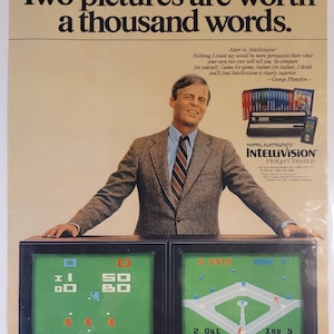 May include: A vintage advertisement for Intellivision, a home video game console, featuring a man in a suit standing in front of two televisions displaying baseball games. The text reads "Two pictures are worth a thousand words." and "Atari vs. Intellivision? Nothing I could say would be more persuasive than what your own two eyes will tell you. So compare for yourself. Game for game, feature for feature, I think you'll find Intellivision is clearly superior. -George Plimpton- "