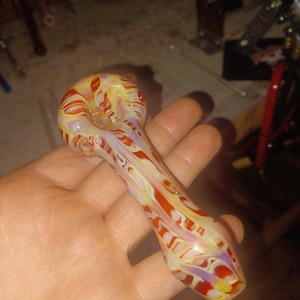 Pode incluir: Um cachimbo de vidro com um padrão de espiral em tons de vermelho, amarelo e branco.