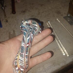 May include: A glass pipe with a white, red, and blue swirl pattern. The pipe has a small bowl at the top and a long, thin stem.