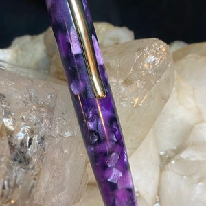 May include: A purple and white marbled pen with gold accents. The pen is made of resin and has a smooth finish.