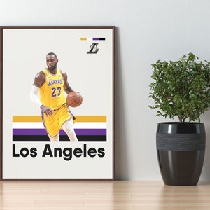 May include: A framed poster featuring a basketball player wearing a yellow and purple jersey with the number 23 and the word "LAKERS" on the front. The player is dribbling a basketball. The poster has a white background with a purple, white, and yellow stripe across the bottom. The words "Los Angeles" are printed in black below the stripe. The poster is framed in a brown frame.