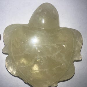 May include: A translucent, light yellow turtle figurine. The turtle is carved with detailed flipper and head features. The figurine is made of a smooth, polished material, and the overall shape is symmetrical.