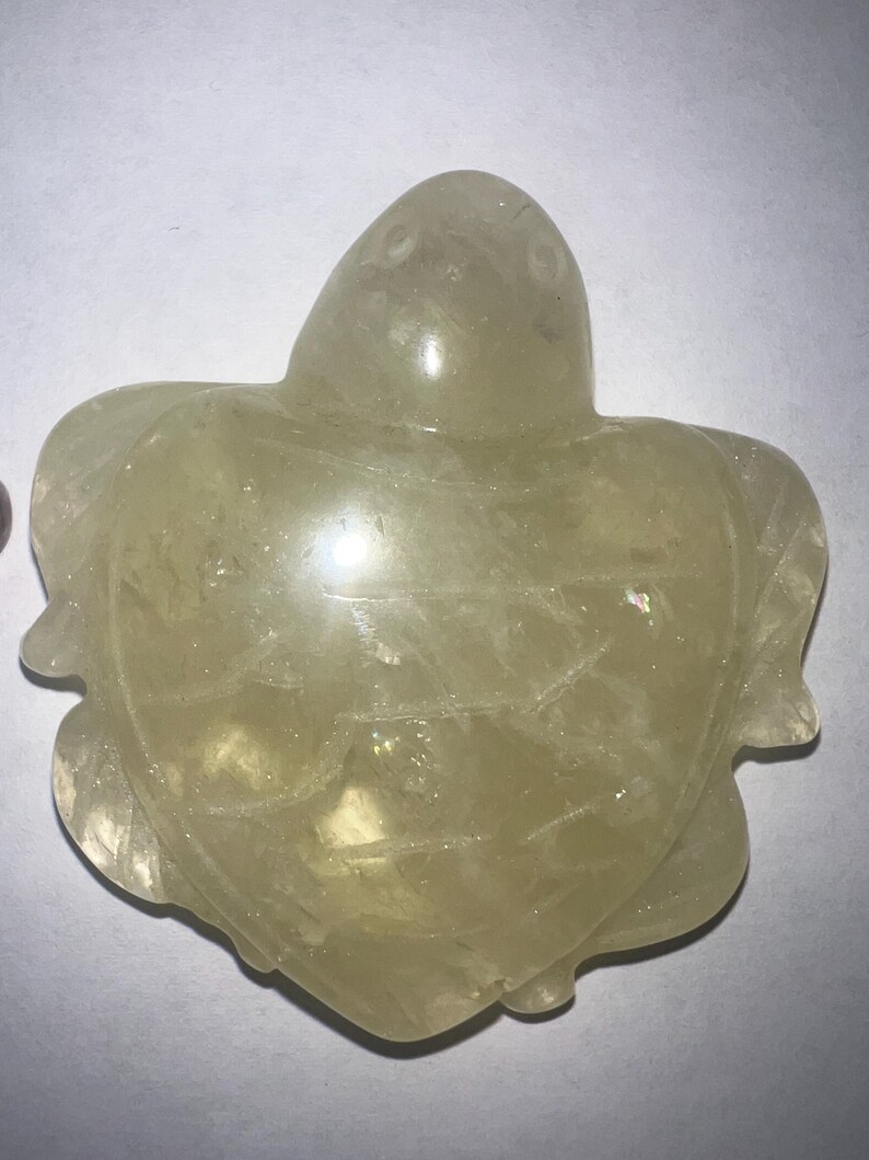 May include: A translucent, light yellow turtle figurine. The turtle is carved with detailed flipper and head features. The figurine is made of a smooth, polished material, and the overall shape is symmetrical.